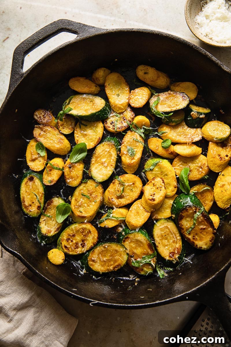 Crispy Zucchini with Aromatic Basil and Pecorino 4 Top-down view of vibrant yellow and green zucchini slices perfectly cooked and sizzling in a cast iron pan, showing their appealing golden texture.