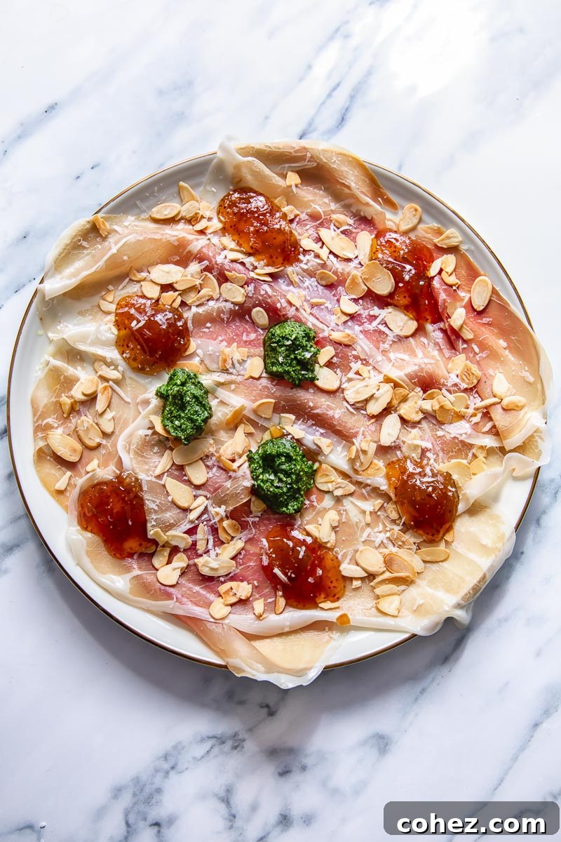 top down view of prosciutto platter topped with dollops of pesto, jam and almonds