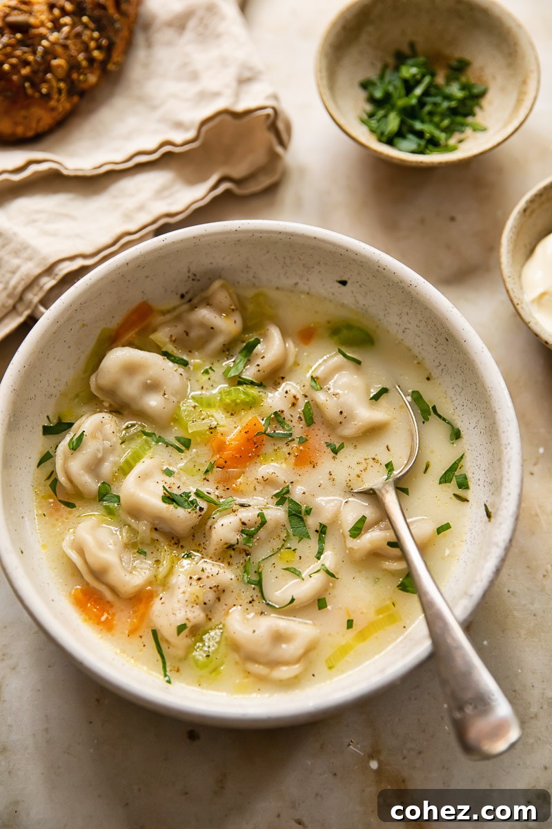 A bowl of Pelmeni Dumpling Soup with a spoon, ready to be enjoyed, garnished with fresh herbs and a swirl of sour cream.