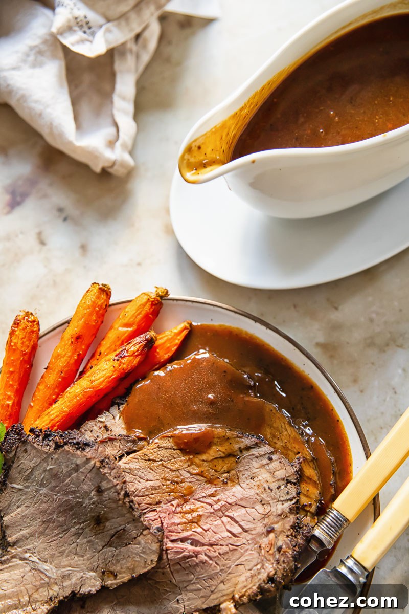Top down view of sliced roast beef with gravy and carrots on a plate, with a gravy boat nearby.