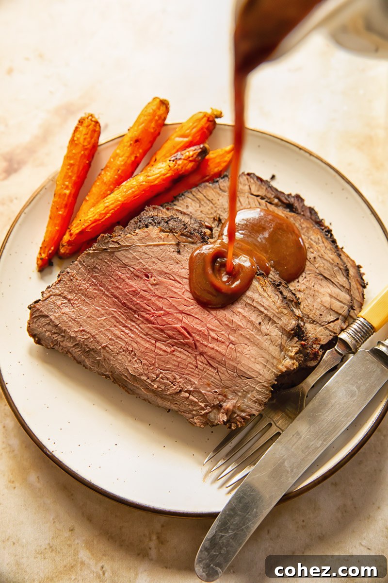 Gravy being poured generously over slices of succulent roast beef on a plate.