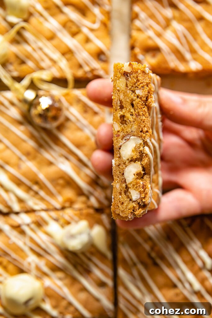 A close-up shot of a hand holding a perfectly baked hazelnut blondie, showing its golden-brown color and chewy texture.