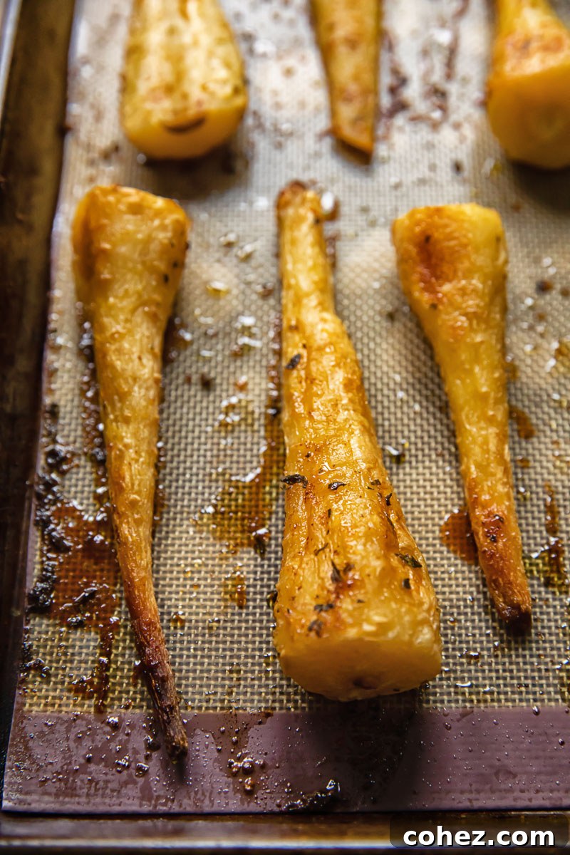 Close-up of golden honey garlic roasted parsnips on a roasting tray, glistening with glaze.