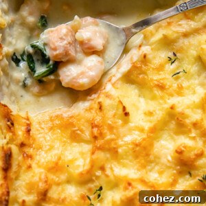 Effortless Fish Pie 6 A bubbling, golden-crusted fish pie with a spoon scooping out a generous portion, revealing chunks of tender fish and creamy sauce underneath the fluffy mashed potato topping.