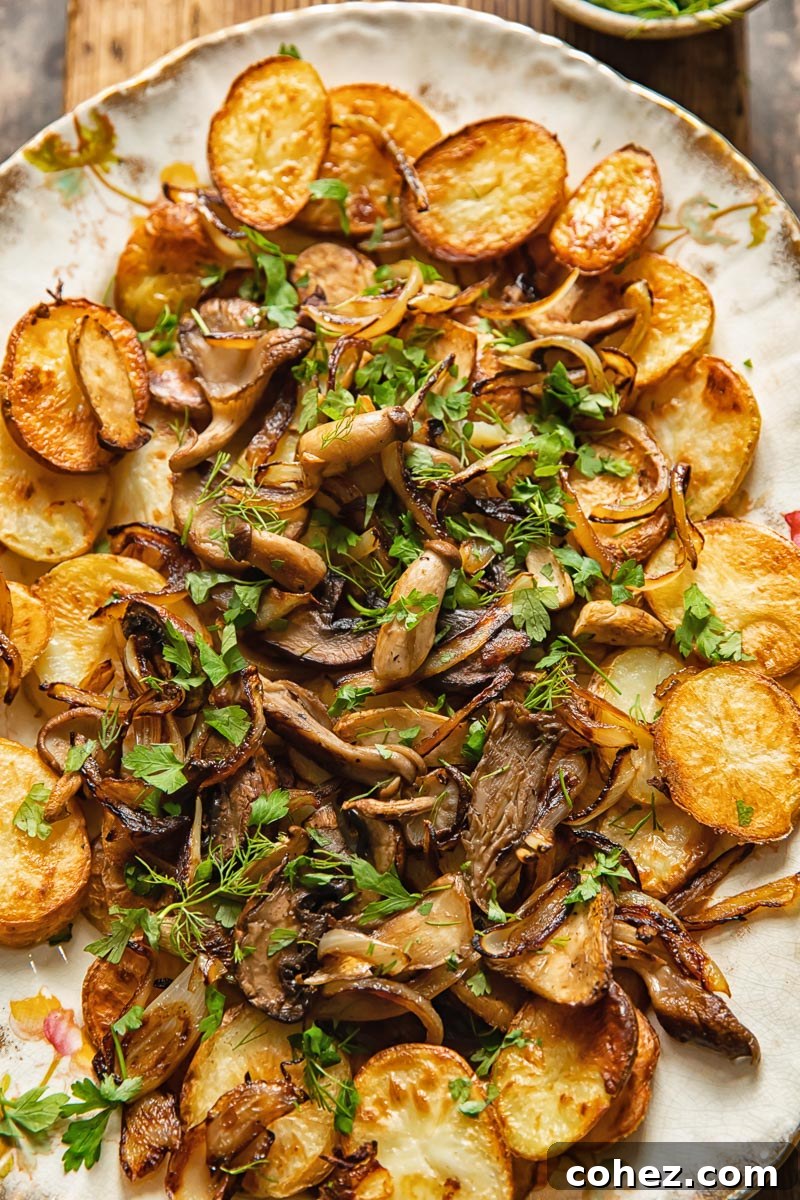 A beautiful serving platter filled with golden fried potato discs, topped generously with savory fried mushrooms and sweet caramelized onions, garnished with fresh herbs.