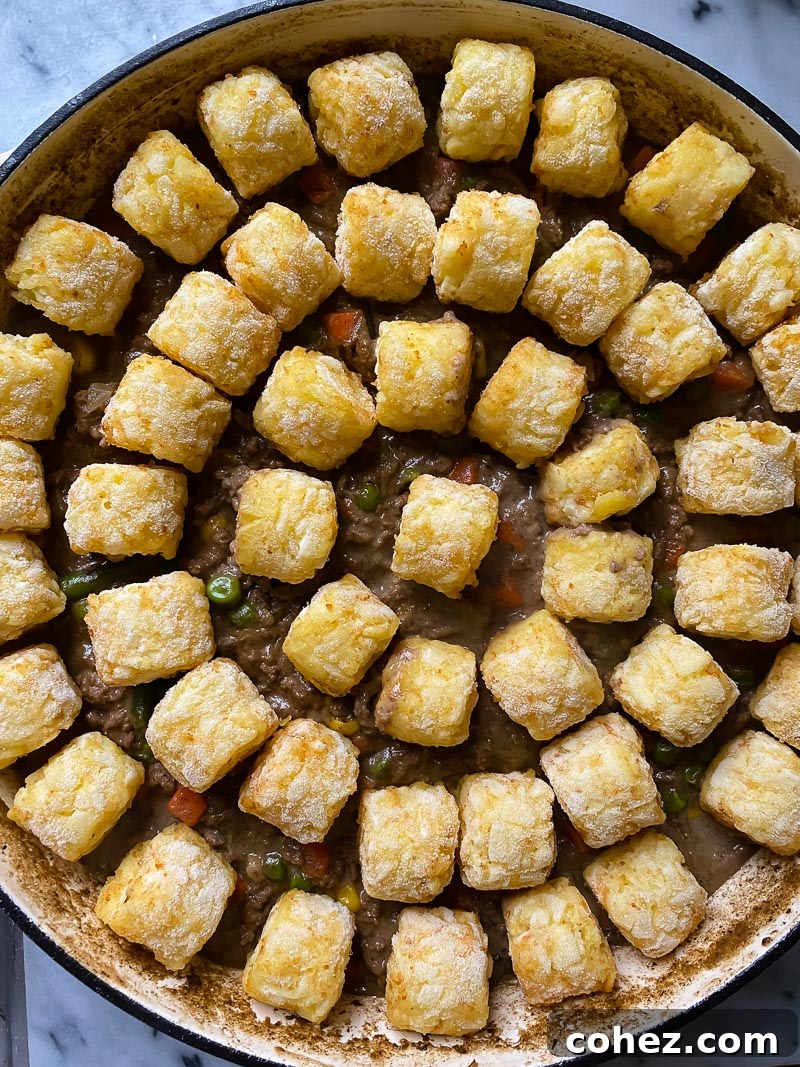 An unbaked Tater Tot Casserole, showing the savory ground beef and vegetable filling topped with a neat layer of frozen tater tots, ready for the oven.