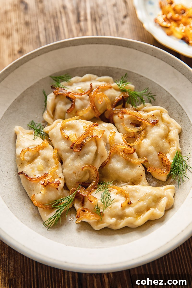 varenyky in a bowl, topped with fried onions and fresh dill