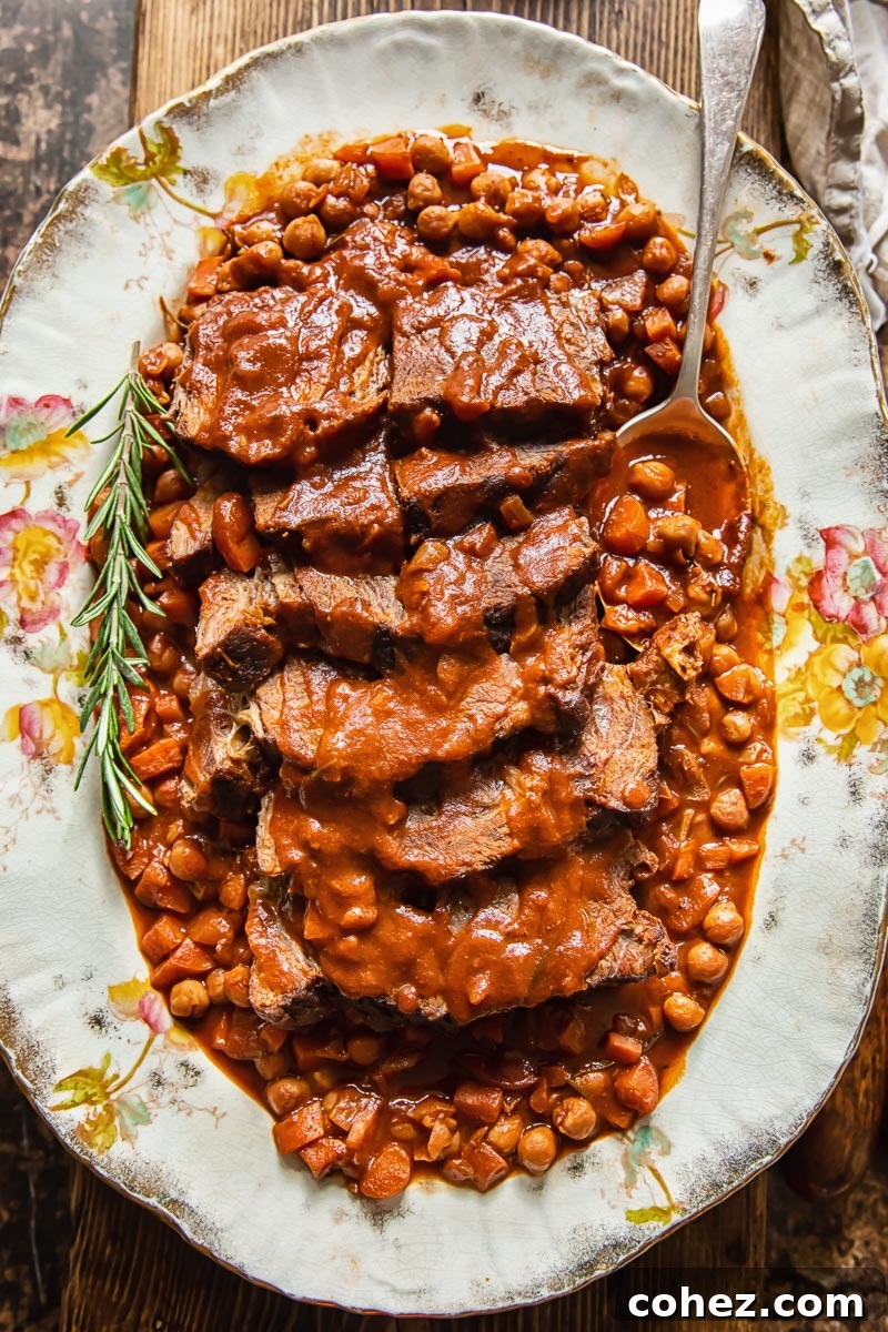 top down view of sliced pot roast with vegetables and chickpeas on a platter, ready to serve