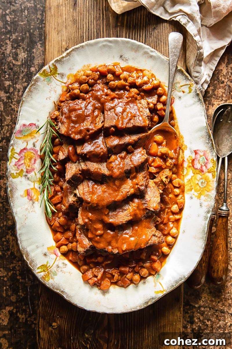 top down view of sliced roast beef with a tomato based gravy and chickpeas, served on a platter