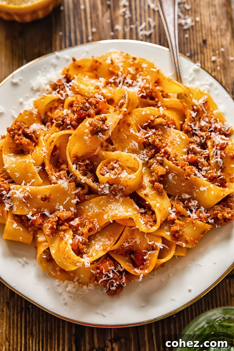 A close-up of pappardelle pasta generously coated with rich Tuscan ragu sauce, served on a white plate with a fork, inviting a taste of Italy.