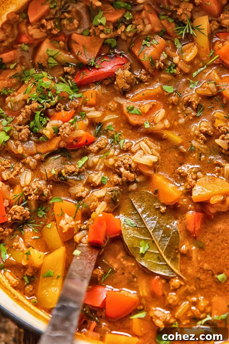 Close-up view of a rich, hearty unstuffed pepper soup with ground beef and rice simmering in a large pot, with a ladle resting inside, ready to be served.