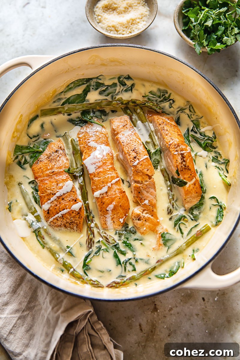 top down view of salmon filets in a creamy sauce with spinach and asparagus