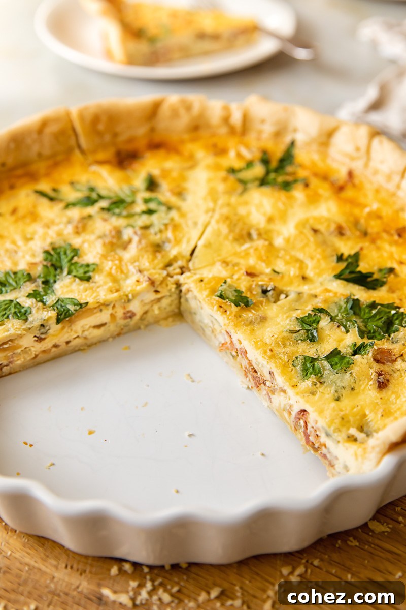 Side view of a freshly baked bacon, blue cheese, and caramelized onion quiche with a few slices already removed, showcasing the rich filling and golden crust.