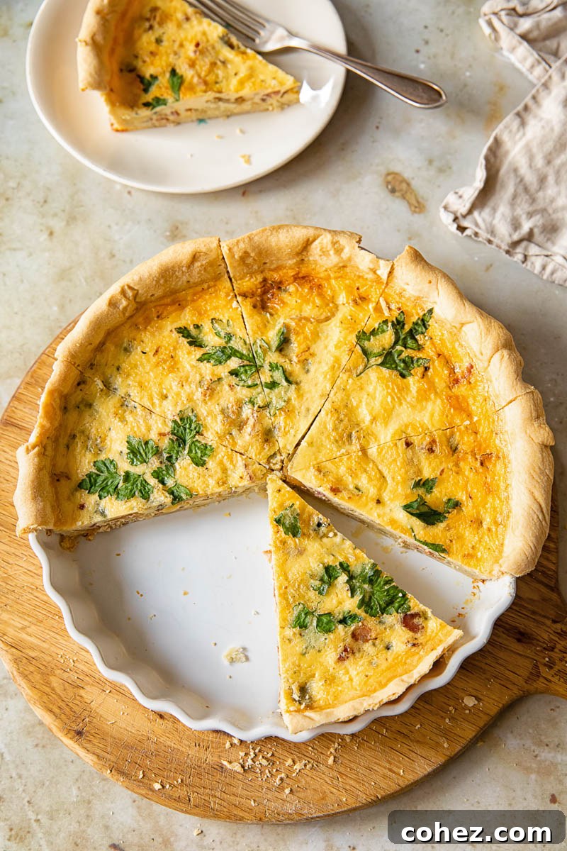 Top-down view of a golden-brown bacon, blue cheese, and caramelized onion quiche with one slice removed, revealing the delicious layers inside.