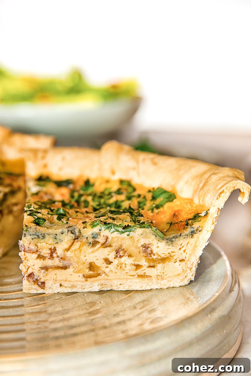 A close-up view of a perfectly baked slice of bacon, blue cheese, and caramelized onion quiche, showcasing its flaky crust and rich filling.