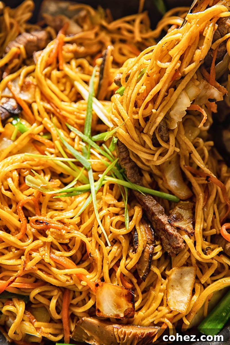 Close-up shot of Japanese noodles being stir-fried in a large pan or wok, showcasing their texture and vibrant color.