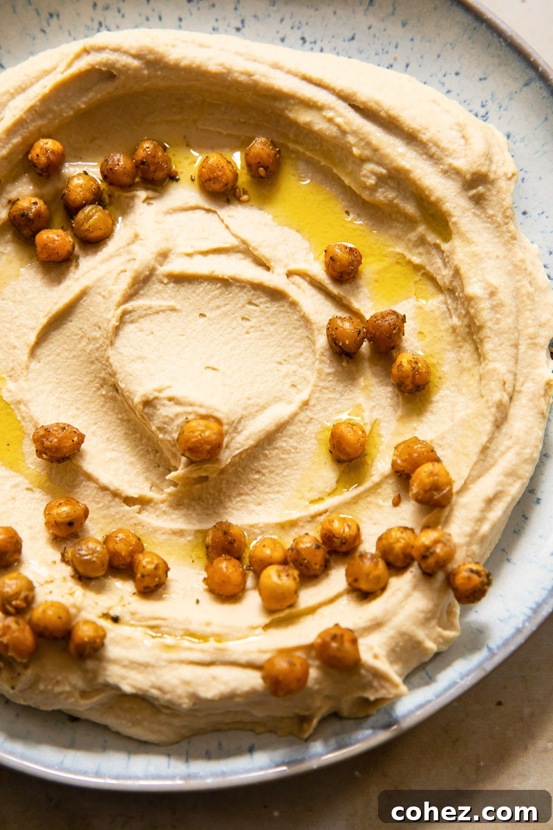 Top-down view of creamy homemade hummus generously topped with golden roasted chickpeas and a swirl of olive oil, ready to be served.