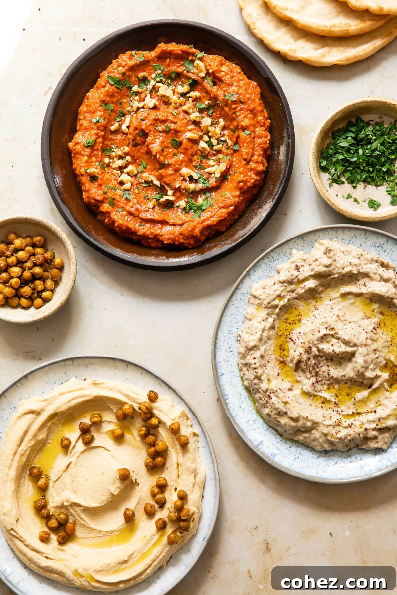A vibrant display of Middle Eastern appetizers: a bowl of homemade hummus, a smaller bowl of crunchy roasted za'atar chickpeas, and a bowl of fresh chopped parsley for garnish.