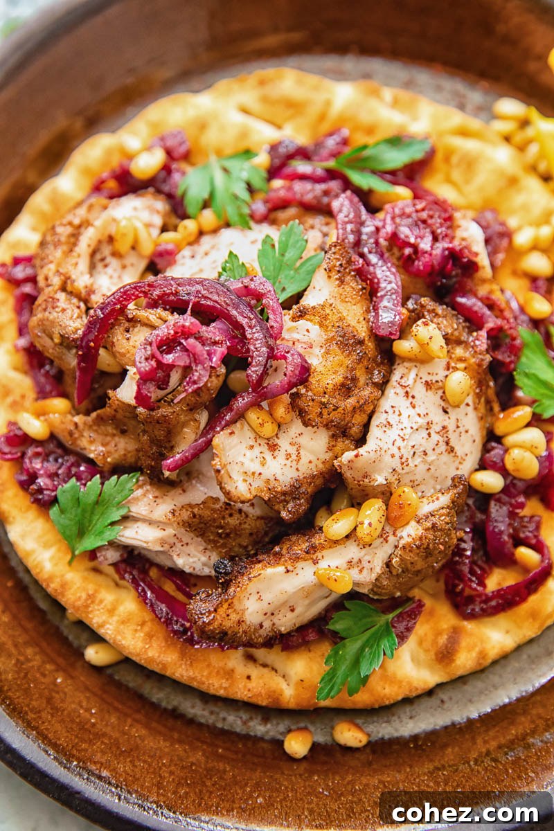 Palestinian Sumac Chicken 2 Close up shot of round flat bread with chicken and red onions on top, showcasing the rich colors and textures of Chicken Musakhan