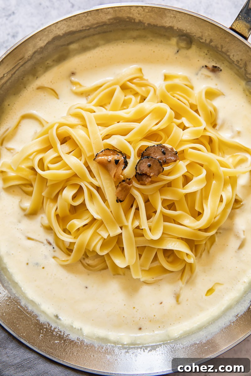 Process shot of tagliatelle pasta being added to truffle sauce in pan