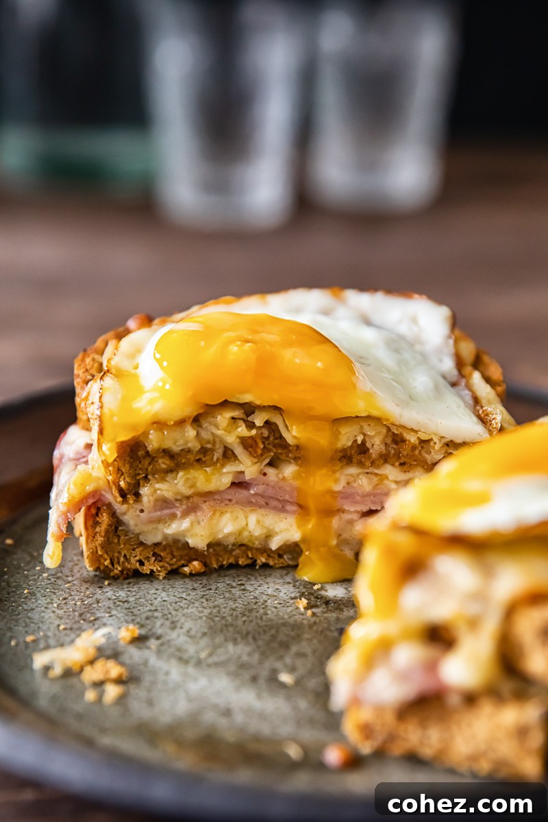 Ultimate Croque Madame 3 A close-up, cross-section view of a Croque Madame, revealing its layers of thick bread, melted Gruyère cheese, and savory ham, with a rich béchamel sauce creating a creamy texture. A golden fried egg rests on top.
