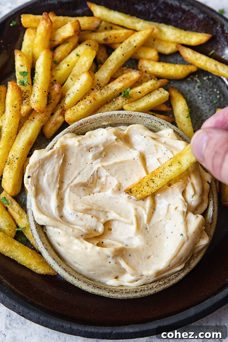 Decadent Truffle Aioli 2 Top down shot of person dipping a fry into truffle aioli dip.
