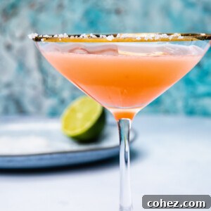 Side shot of blood orange margarita in a cocktail glass next to a lime