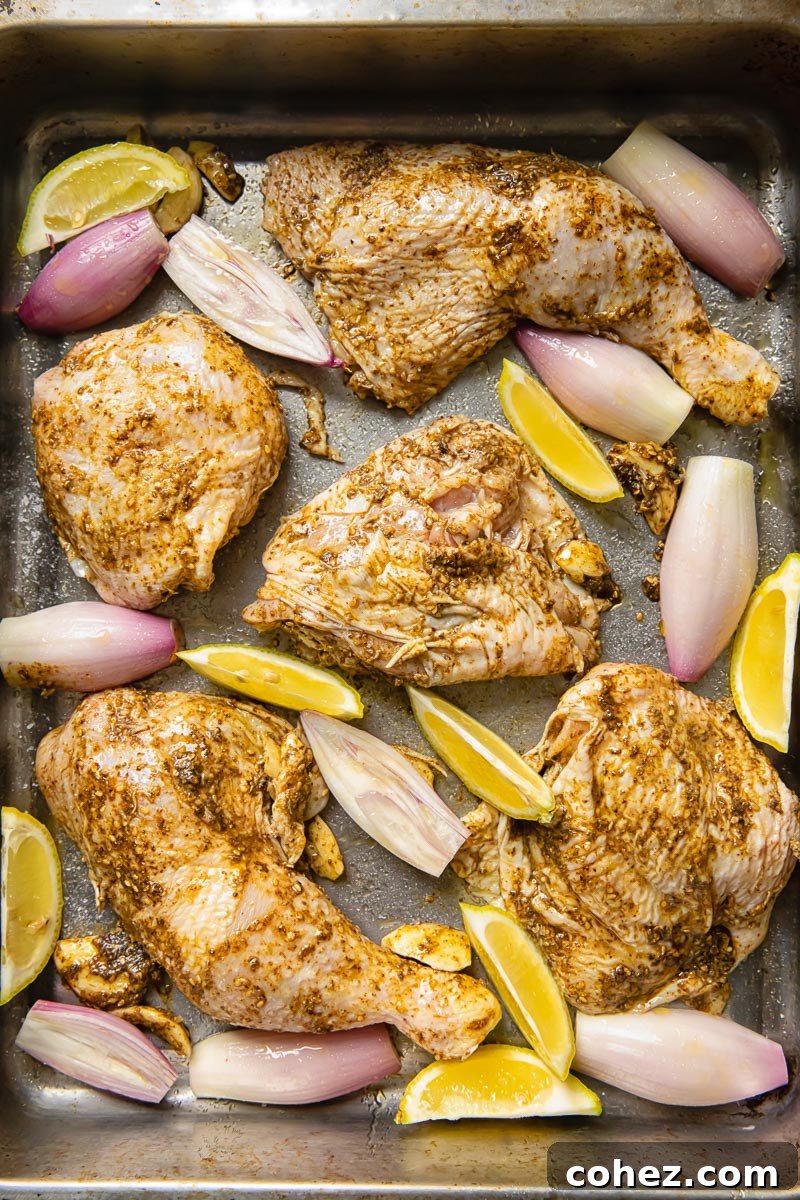 Process shot of chicken thighs and legs on a baking tray before being cooked, coated in za'atar marinade.