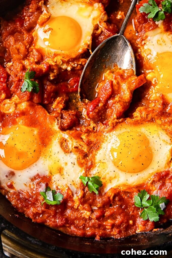 Close-up, top-down shot of shakshuka in a pan, showcasing the vibrant tomato sauce and perfectly cooked eggs.