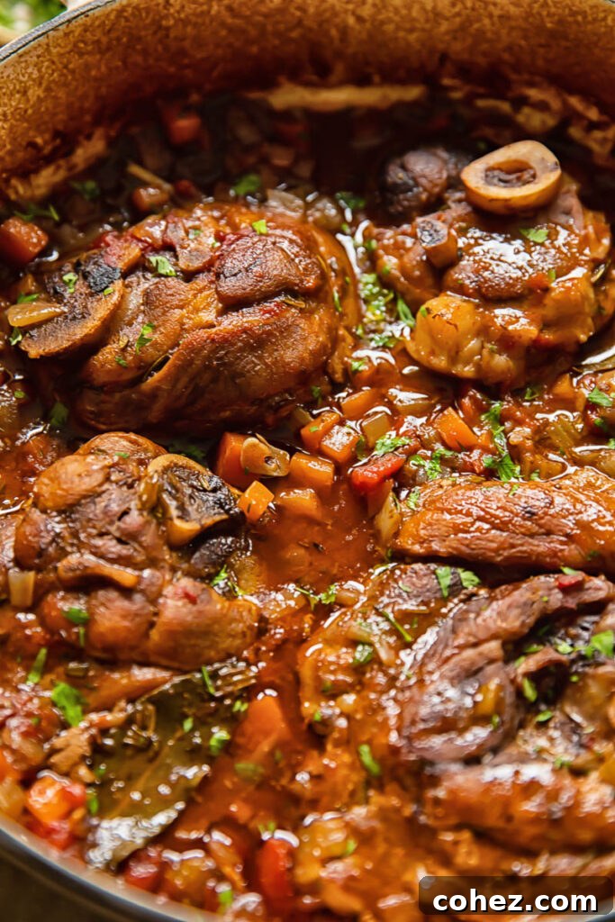 Close up shot of Pork osso buco simmering in a pot with cut up carrots, celery, and herbs