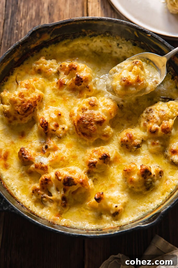 Top down view of a spoon scooping a bite of creamy cauliflower gratin from a cast iron pan.