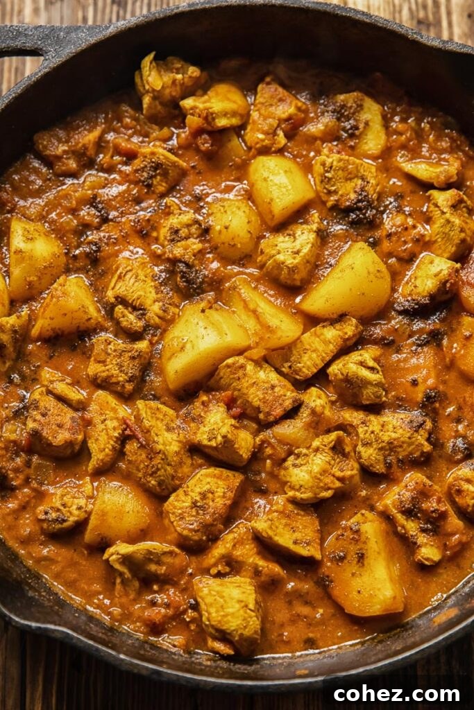 A close-up view of the simmering chicken curry with potatoes in a cast iron pan, ready to be served.