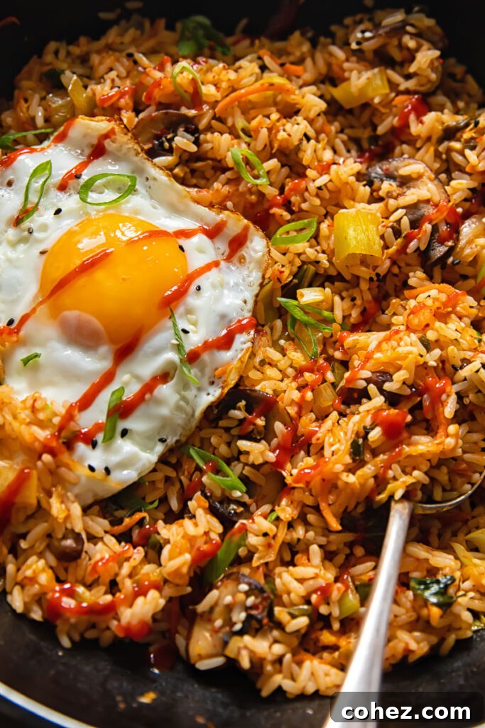 Close-up view of Kimchi Fried Rice adorned with a sunny-side-up egg, glistening sesame seeds, and fresh green onions.