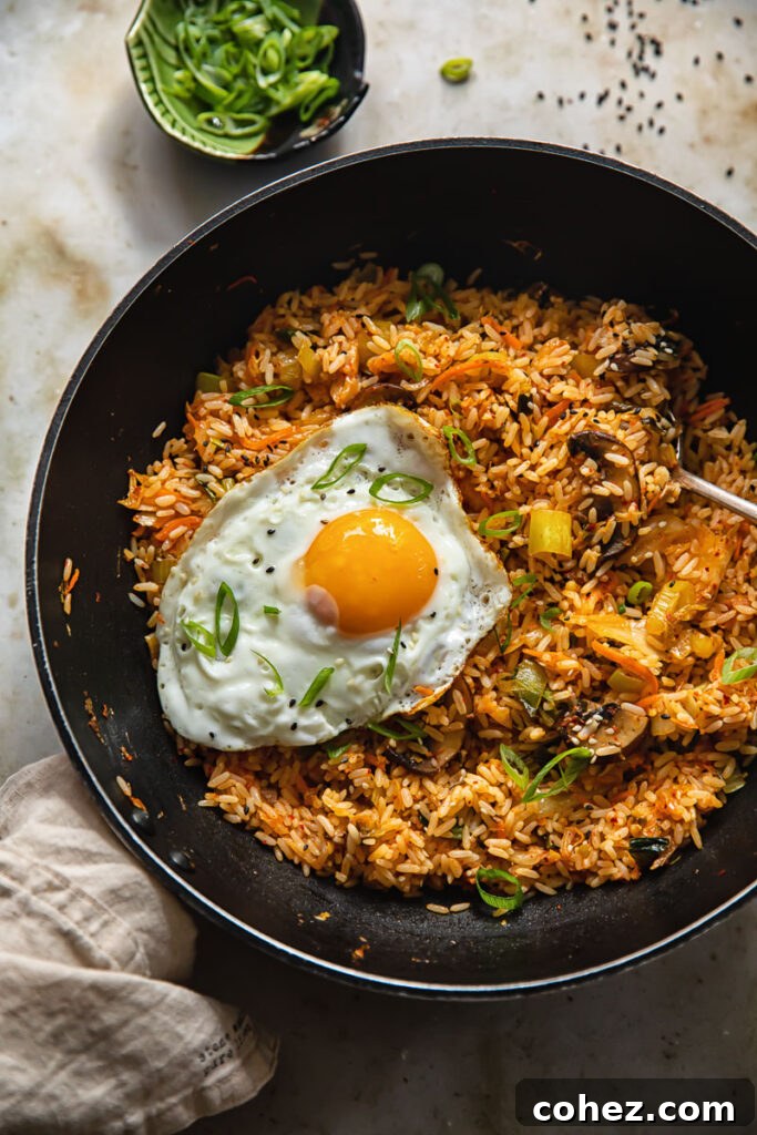 A wok of freshly cooked Kimchi Fried Rice with a fried egg, alongside a small bowl of sliced green onions, ready for garnish.