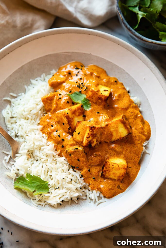 Serving bowl of creamy paneer tikka masala next to a bowl of fluffy white rice, garnished with fresh herbs.