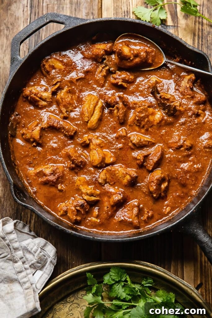 Overhead view of a cast iron pan filled with bubbling chicken Rogan Josh, placed on a rustic wooden table