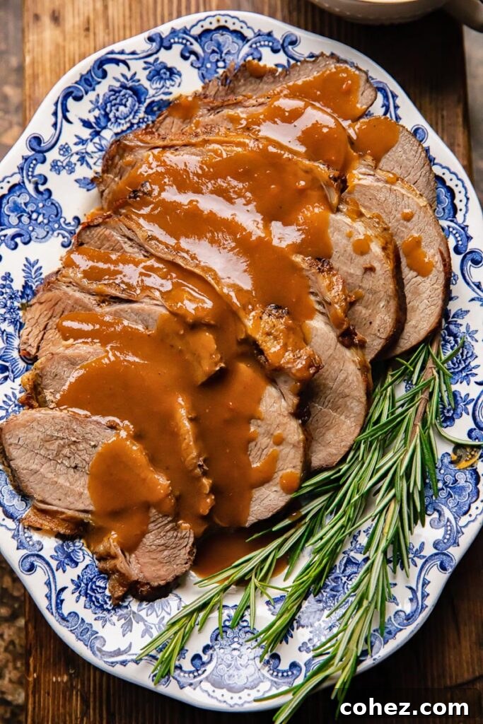 Fall Apart Slow Cooker Roast 2 Top down shot of slow cooker roast beef on a plate with rich gravy and fresh rosemary garnish
