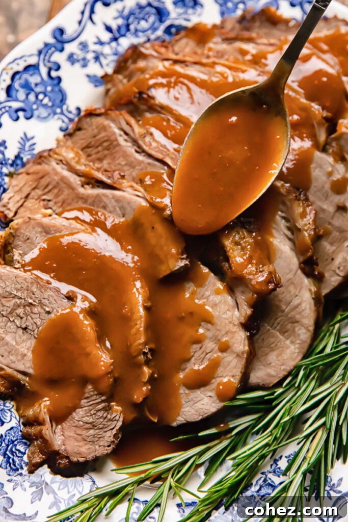 Fall Apart Slow Cooker Roast 3 Close-up of rich brown gravy being poured over slices of slow cooker roast beef garnished with rosemary