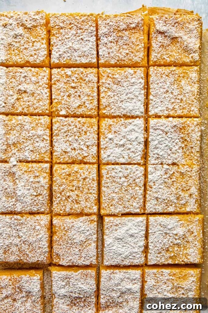 Zesty Lemon Squares 3 Top-down shot of a baking sheet filled with golden lemon bars, freshly baked and being cut into neat pieces, ready to be enjoyed.