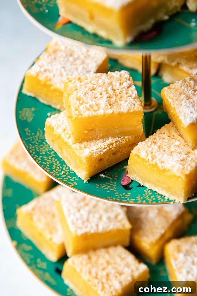 Zesty Lemon Squares 4 Side shot of many individual lemon bar pieces, generously dusted with powdered sugar, arranged artfully on a white platter.