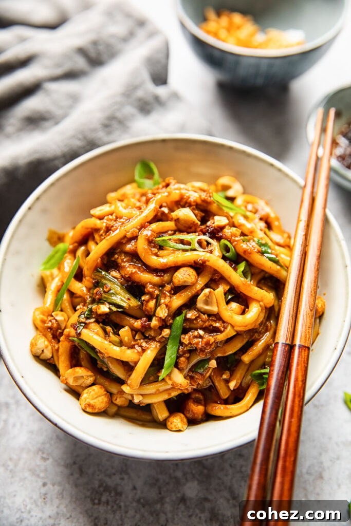 Top down view of a bowl of Vegan Dan Dan Noodles with chopsticks, showcasing the rich sauce, noodles, and garnishes.