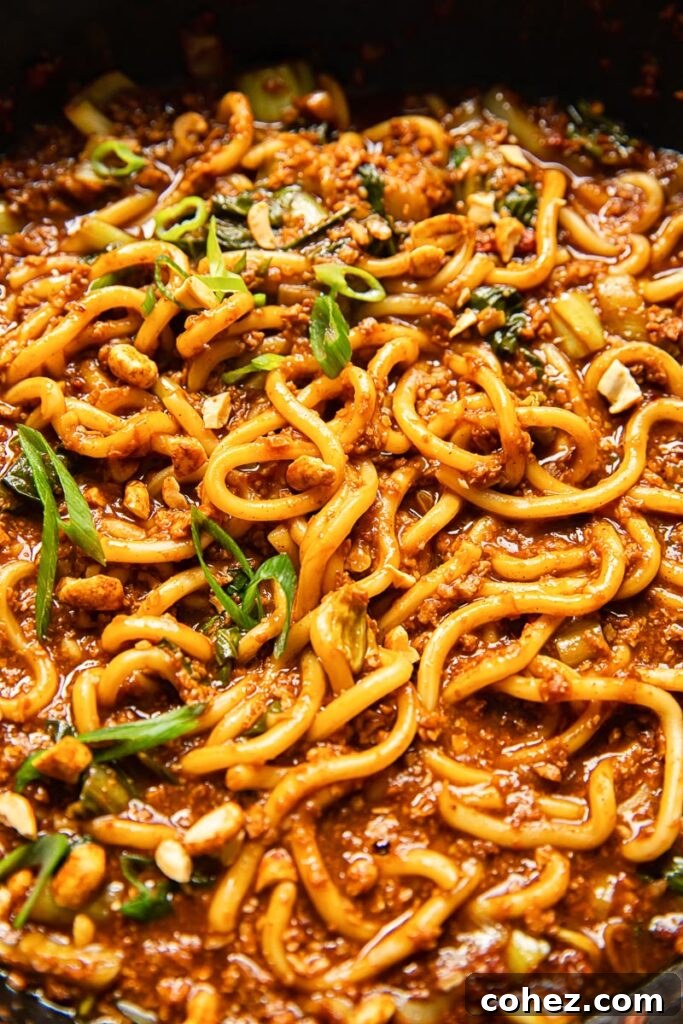 Close-up shot of vegan Dan Dan Noodles, highlighting the texture of the plant-based 'meat' and vibrant greens.