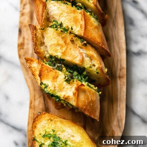 Top down shot of slices of garlic bread layered next to each other on a cutting board, garnished with fresh parsley.