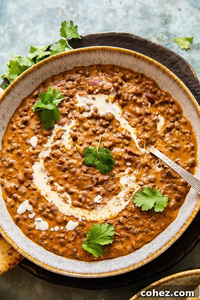 A bowl of creamy Dal Makhani garnished with fresh cilantro, a spoon rests in the dish, highlighting its rich texture.