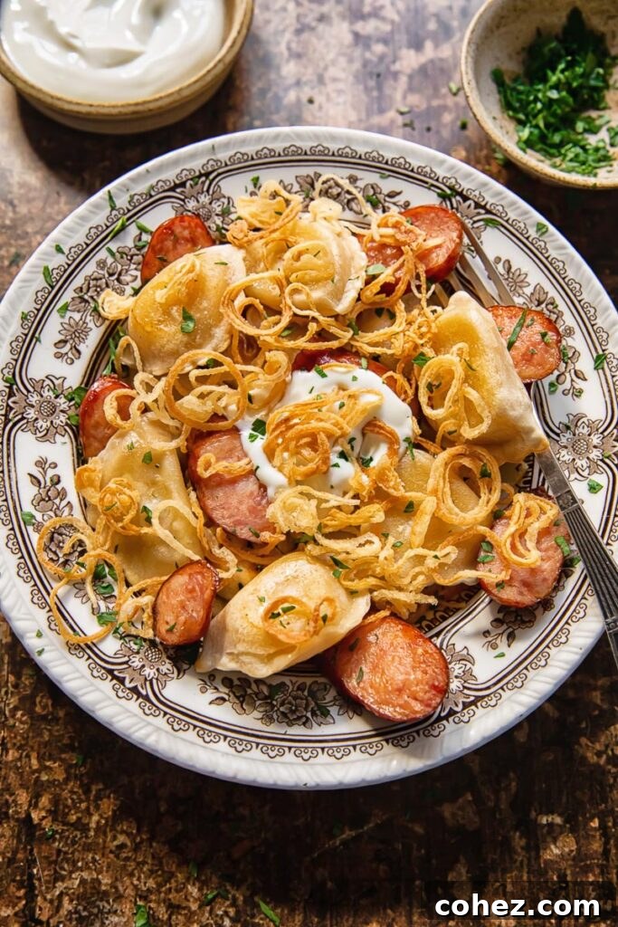 Top down shot of pierogies and kielbasa in a bowl with a fork and a dollop of sour cream on top