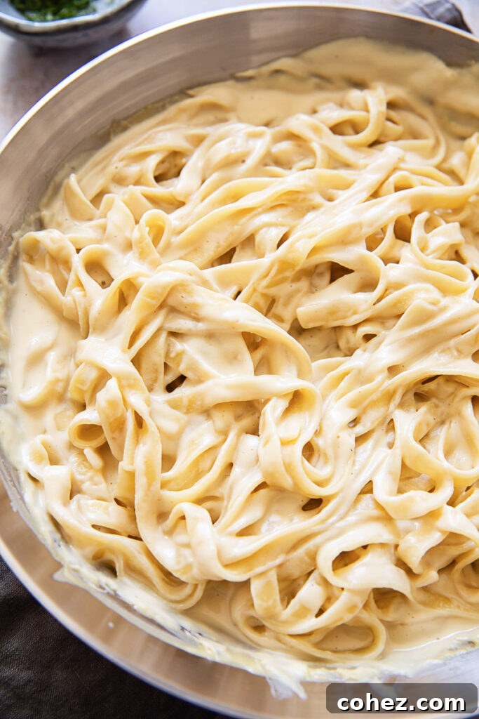 A bowl of tagliatelle pasta generously coated in a creamy cashew Alfredo sauce, garnished with fresh herbs.