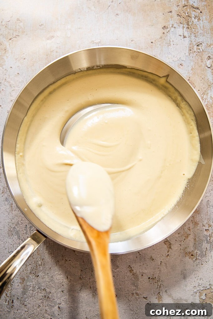 A bowl of creamy vegan Alfredo sauce with a spoon lifted, showing its smooth and thick consistency.