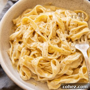 Bowl of vegan Alfredo sauce with sprinkling of pepper and a fork, serving as the recipe image.