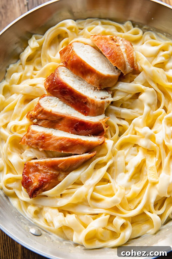 Top down shot of sliced prosciutto wrapped chicken on top of fettucine in alfredo sauce in a bowl