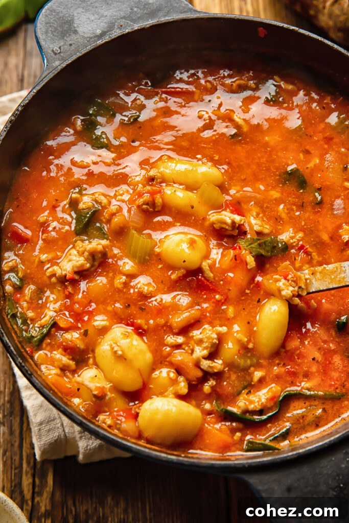 A large pot of Firecracker Sausage Gnocchi Soup with a ladle resting inside, ready to be served.